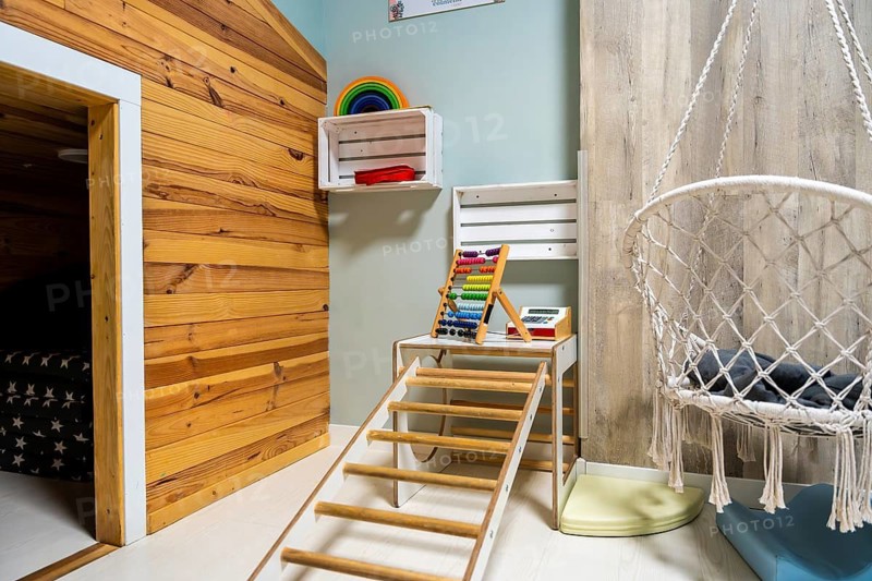 Bright modern children's playroom with wooden climbing frame, abacus, rainbow stackers, playful cash register and cozy macrame swing chair for imaginative learning and playroom fun