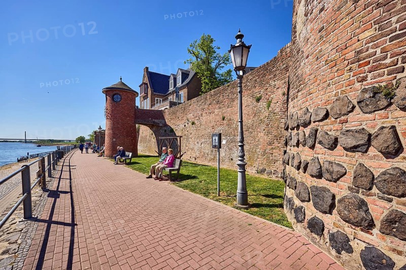 Rhine river, general architecture, houses, brick wall, Rhine level Rees, level tower, metal railing, waterfront, footpath, lantern, benches, lawn, tree, walkers and seated people as side motifs, blue sky, cloudless, Rhine promenade, Rees, Kleve district, North Rhine-Westphalia, Germany