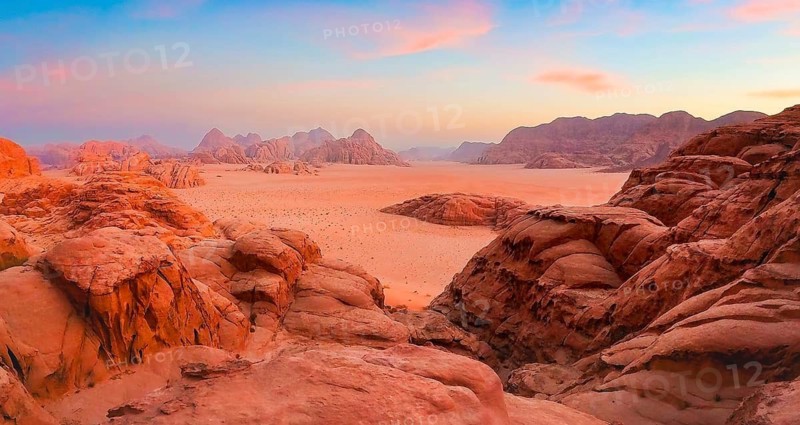 Aerial panoramic view orange Wadirum desert sand valley rock formations sandstone mountains horizon colorful pink blue twilight sunset sky wilderness landscape Wadi Rum Jordan