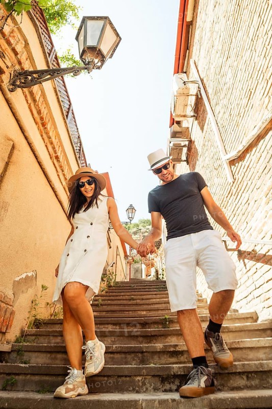 Couple young tourists walking down old stairs sightseeing old Tbilisi streets at holiday - Happy friends laughing together on vacation - People and holidays concept. Travel in Georgia