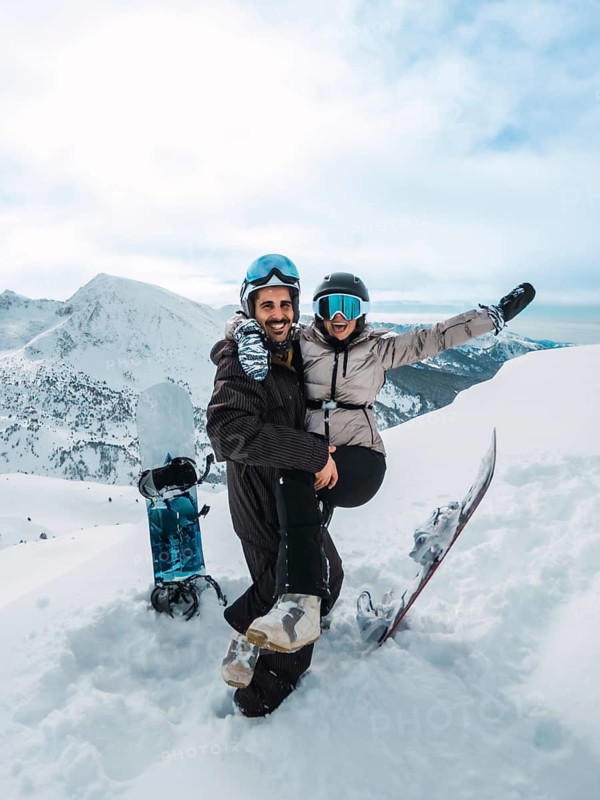Young couple embracing and laughing on a snowy mountain summit with snowboards, enjoying an adventurous winter vacation of love, freedom and active outdoor fun
