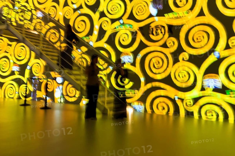 Swirling patterns, spirals, gold, yellow, immersive exhibition, digital art, colorful projections on walls and floors, Gustav Klimt, visitors, silhouettes, motion blur, art museum, Port des Lumieres, Westfield Überseequartier, Hafencity, Hamburg, Germany