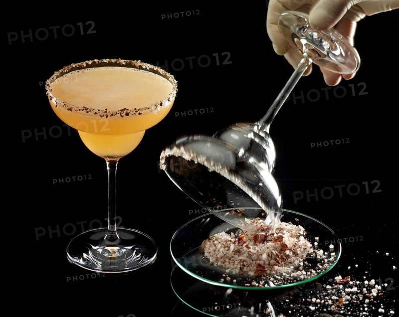 Orange-colored cocktail on a black background, salt rim as a garnish, glass with salt rim is prepared next to it, studio recording