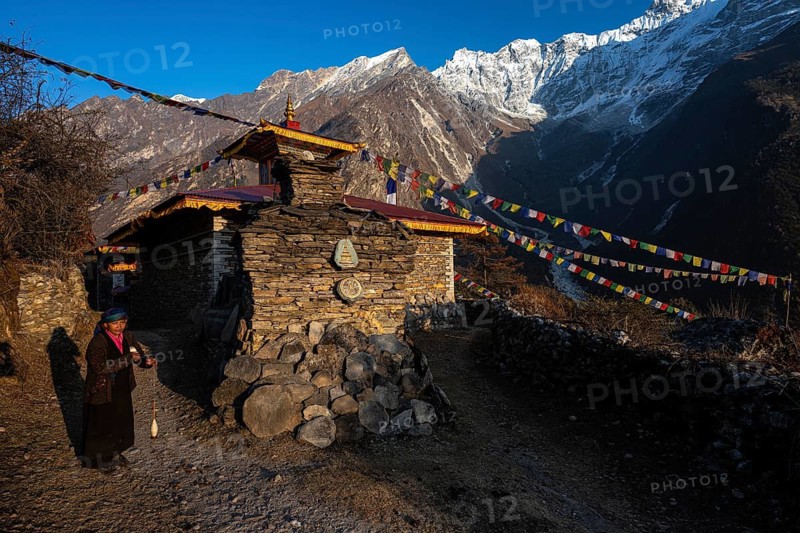 Young woman next to a small Buddhist monastery with manistones in the evening light, Nepalese, local of the Tsumba Tibetan ethnic group traditionally spinning wool with a spindle, Tsum Valley, Himalayas, Nepal