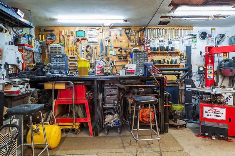 Cluttered home garage workshop showing workbench, parts drawers, various tools and machines including RockSolid RSC4000 swing arm tire changer, Quebec, Canada