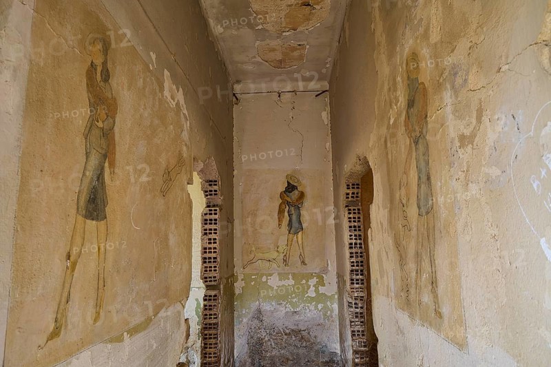 A narrow corridor with faded vintage style murals surrounded by shabby old walls, Lost Place, Tourtouras Mountain, Coastal Battery, WW2, World War II, German Coast Battery PL 388, Marine Artillerists, Wall Mural, Graffiti, Painter presumably Otto Meister, Diapori, Xirokambos, Leros, Dodecanese, Greek Islands, Greece
