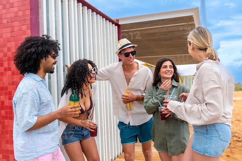Diverse group of young adult friends laughing and talking together while holding refreshing drinks at a casual outdoor summer party, embracing friendship and a relaxed social lifestyle