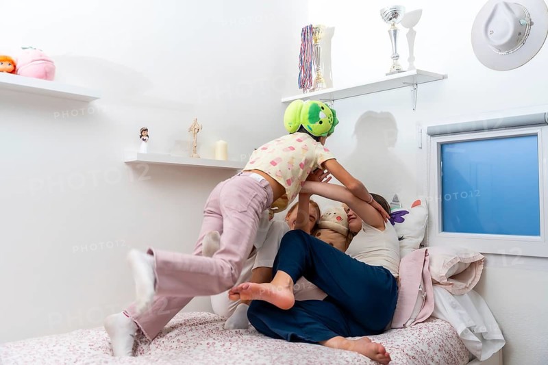 Young sisters actively playing home on a bed in their bedroom, enjoying a joyful moment of playful wrestling, embodying concepts of childhood, family bonding, and candid fun