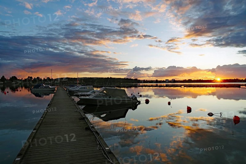 Beautiful sunset over a harbor with calm water and a few boats along a wooden pier, Karlsborg, Västra Götalands län, Sweden