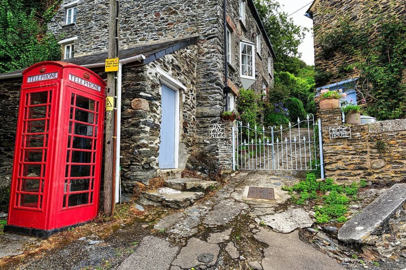 Red telephone box on a paved path next to a historic stone house, cottage, iron gate, Portloe, fishing village on the Roseland Peninsula, England, United Kingdom