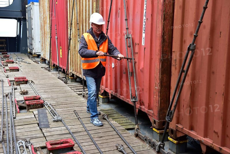 Worker with helmet secures containers on the bottom of the harbor with tension ropes, workers on tie rods on a container ship, Schleswig-Holstein, Germany