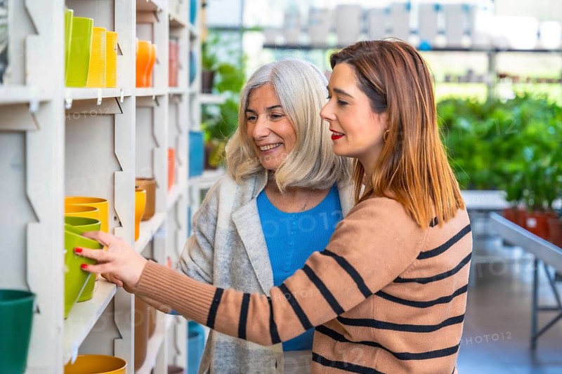 Mother and daughter smiling as they browse colorful ceramic plant pots on shelves in a garden center, enjoying shopping, gardening hobby and cheerful bonding time together