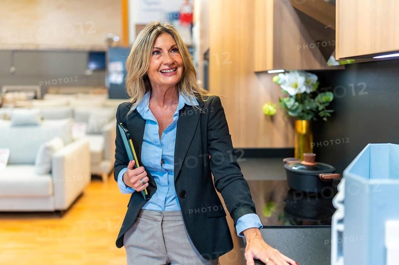 Professional female interior designer looking at new kitchen installations in a modern home improvement store, holding a folder and planning a renovation project