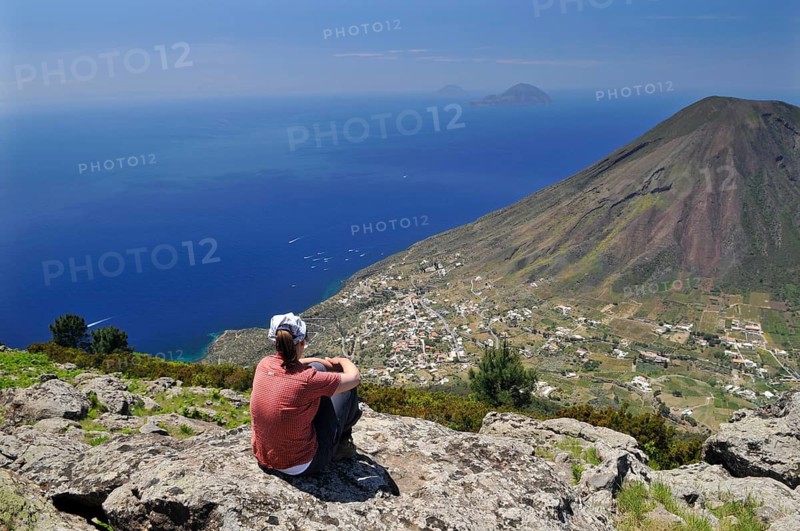 Woman sitting on a rock looking towards Filicudi and Alicudi, Salina, Aeolian or Lipari Islands, Sicily, Southern Italy, Italy