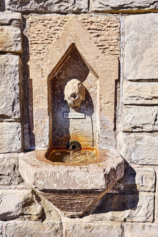 Wall fountain, public drinking water dispenser, sculpture of a fish, sandstone wall, sunny, Bismarckplatz, Meersburg, Lake Constance, Lake Constance District, Baden-Württemberg, Germany