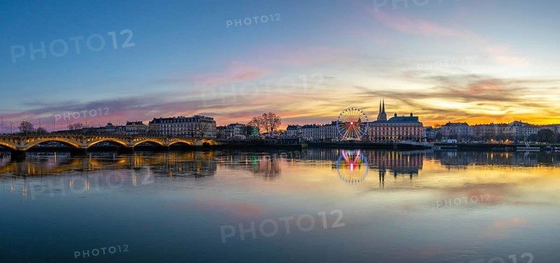 Bayonne cityscape along the adour river at sunset, colorful reflections, illuminated pont saint esprit and festive ferris wheel lighting the riverside during the christmas season
