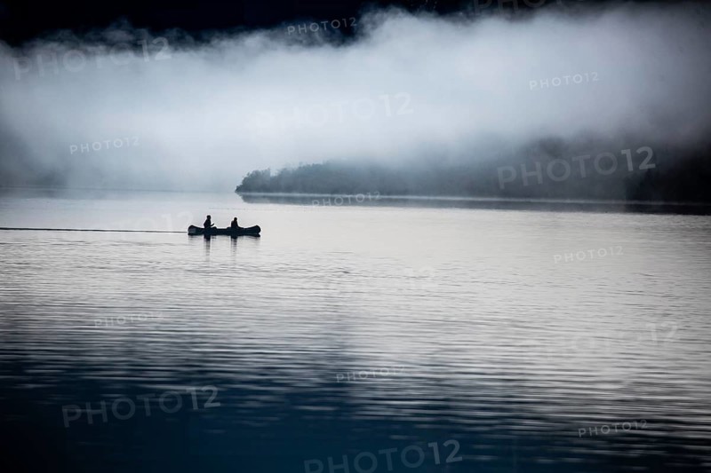 Two people in a boat on a calm lake surrounded by fog, two kayakers paddle in the morning in fog on Aurlandsfjord in Norway