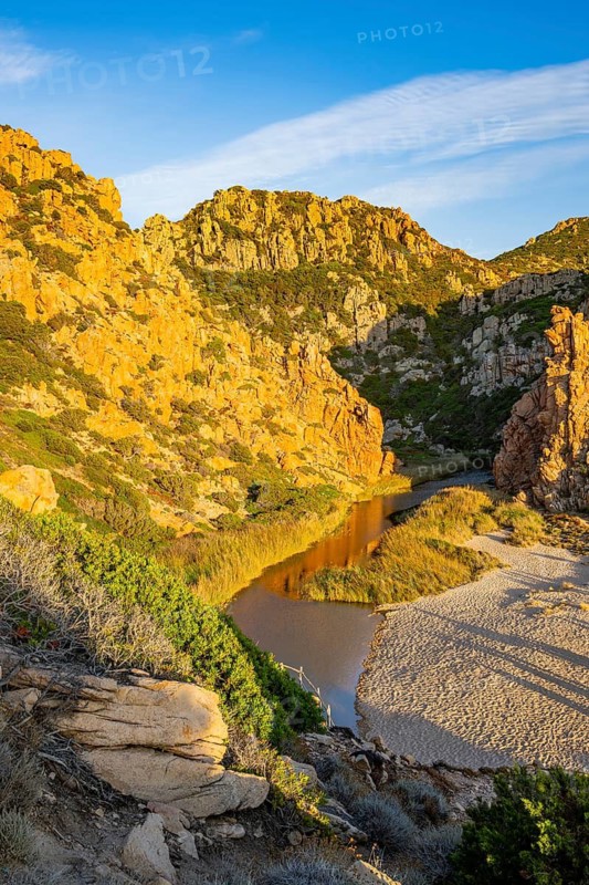 A small river flowing through the mountains into the sea, past a sandy beach in Costa Paradiso on a sunny evening, Sardinia, Italy