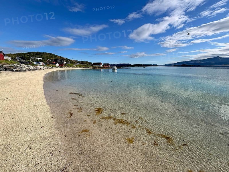 A quiet sandy beach with clear water and a few houses on the shore under slightly cloudy sky, Sommaroy, Sommarøy, Troms, Norway
