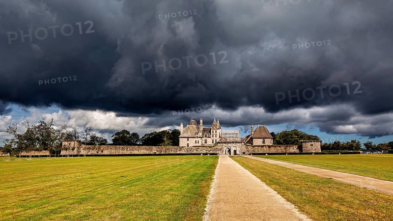 A castle under a looming sky with stormy clouds and an open lawn, The Château de Kerjean Castle in Brittany