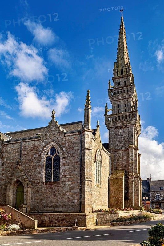 Historic Gothic church with high tower and decorated details under a clear blue sky, Saint-Edern church in Plouédern in Brittany