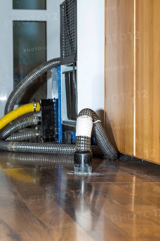 Professional water damage repair Drying equipment and hoses for underbody drying on wooden floor laminate