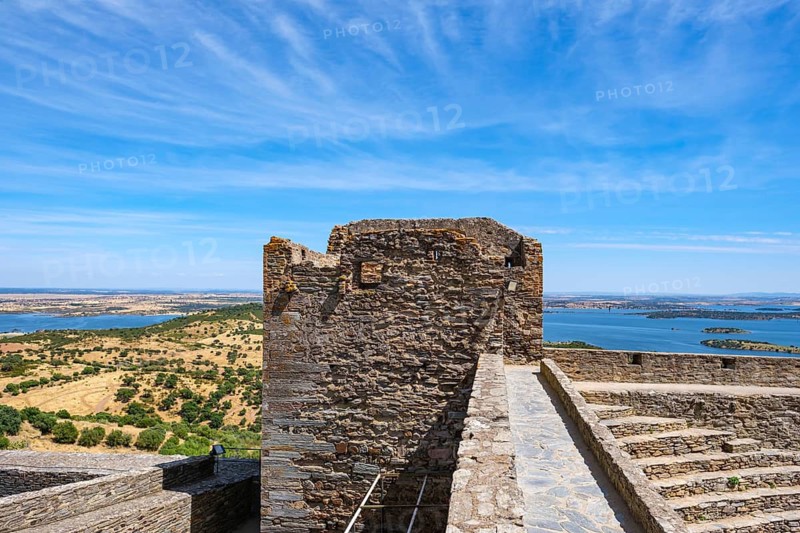 Old stone wall with tower and wide views of countryside and water under blue sky, Monsaraz, Évora, Portugal