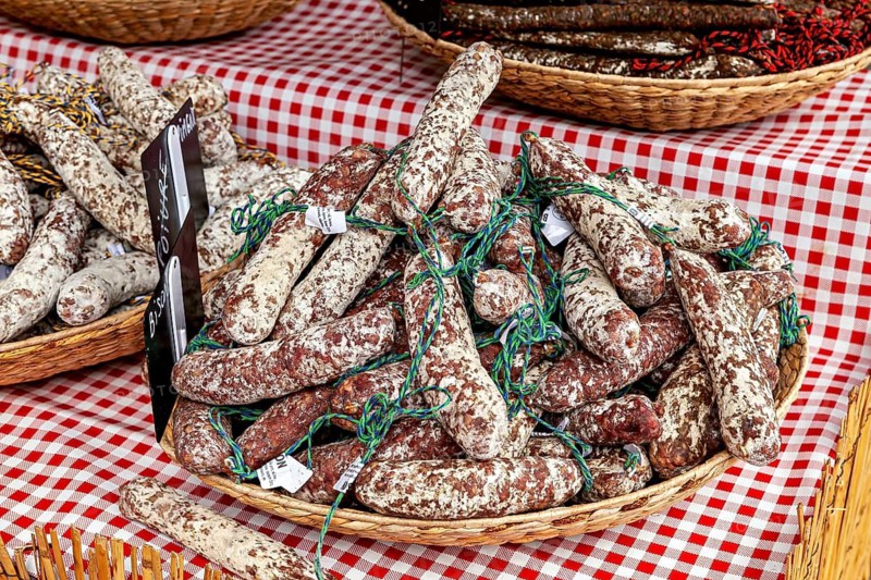 A basket of curled salamis on a red and white checkered table at a market, market stalls in Brittany