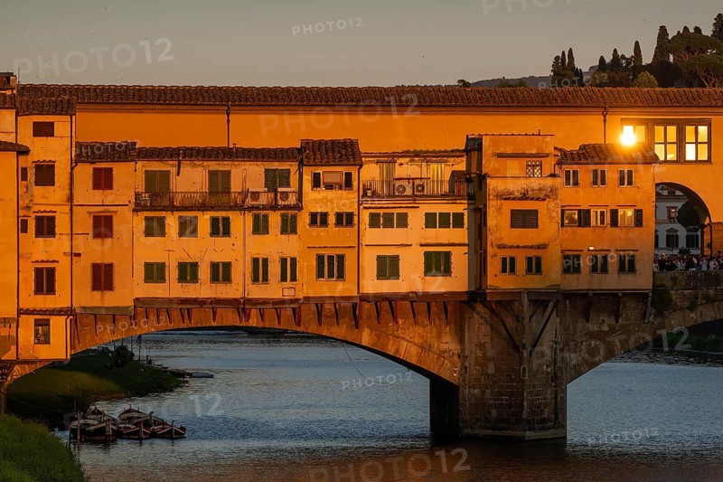 Warm evening light falls on the historic Ponte Vecchio segmental arch bridge across the Arno River and is reflected in window panes, evening mood, old town, Florence, Tuscany, Italy