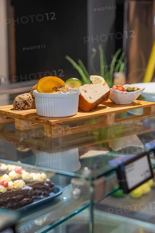 Different types of bread and spreads on a wooden tray in a modern glass display case, breakfast at Cafe Kuh, Deckenpfronn, Germany