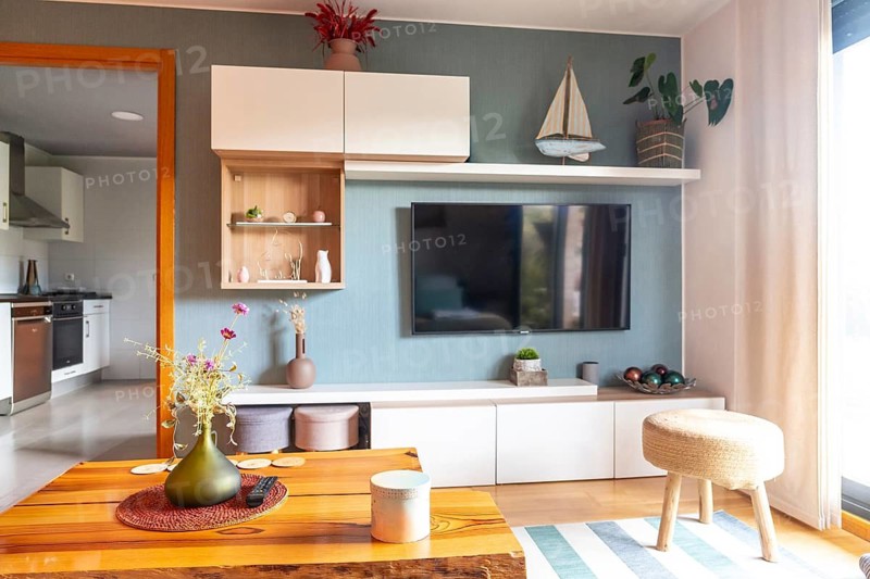 Contemporary living room featuring a wall mounted television. Wooden coffee table. White furniture. Colorful decorations. And a subtle view into the kitchen. Creating a warm. Inviting home environment