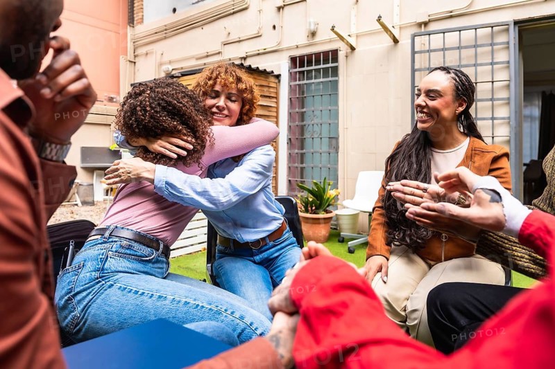 Diverse people gathering outdoors, sitting in a circle, and embracing, symbolizing community support, healing, and recovery during a group therapy session