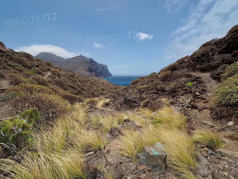 Grassy, barren landscape with sea views and mountains under slightly cloudy sky, La Aldea de San Nicolas, Gran Canaria, Spain