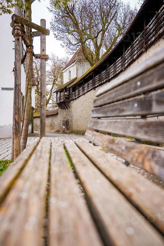 Empty wooden bench in front of a long, arched stone structure in a rural area, Isny, Allgäu, Bavaria, Germany