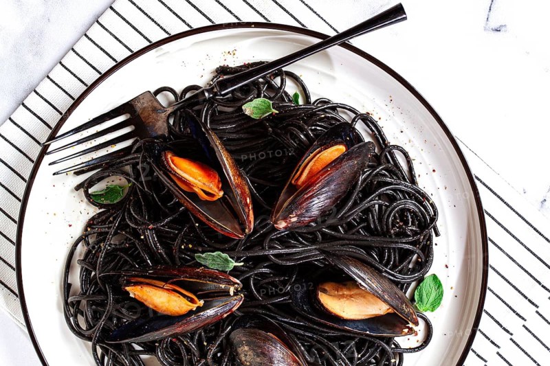 Black spaghetti with mussels, on a white plate with a fork, on a striped napkin, marble background, homemade, no people