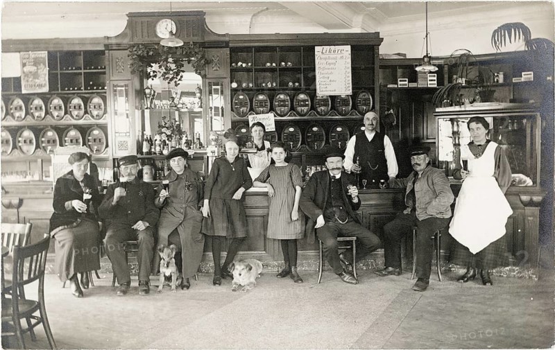 Guest room, pub, restaurant, group sitting happily at a bar with beer barrels in the background, around 1920