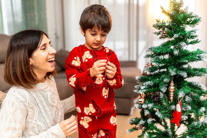 Happy mother and young son spending quality time together, decorating a festive christmas tree in their living room, celebrating a joyful holiday tradition