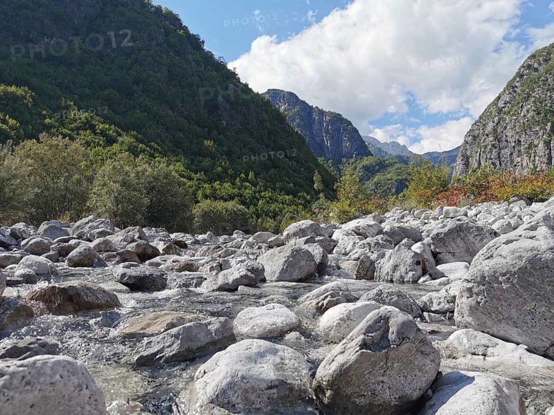 View over a rocky riverbed in a green valley with mountains and cloudy sky, hiking in the Albanian Alps National Park, Albania