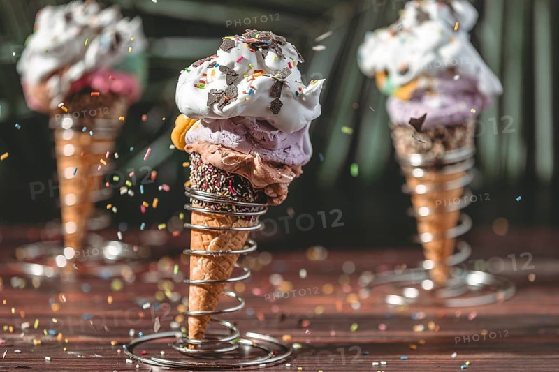 Sprinkles fall on colorful ice cream in waffles in metal holders with cream and