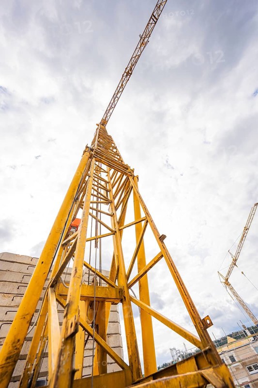 Yellow construction crane rising into the cloudy sky, photographed from a frog's eye view, residential building renovation, Nagold, Calw district, Germany