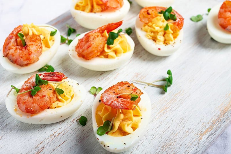 Boiled eggs stuffed with yolk and seasoned with mayonnaise, stuffed eggs with shrimp, on a white wooden chopping board, selective focus, close-up, without people