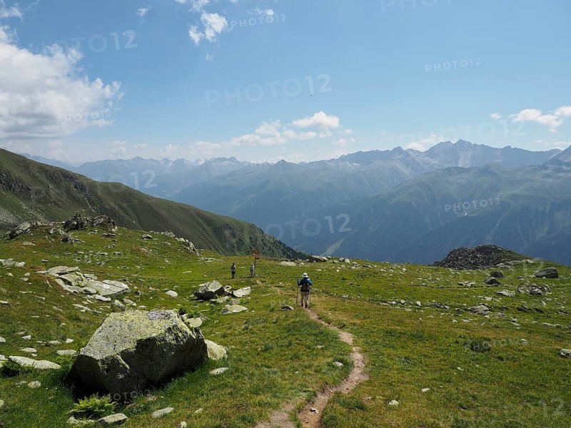 Female hiker on a trail with a wide view of green mountain landscapes and peaks on the horizon, Bellwald, Goms, Canton of Valais, Switzerland
