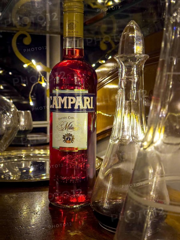 Campari bottle with carafe on wooden counter, evening mood