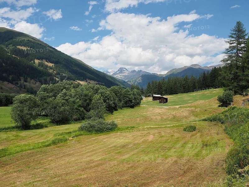 A wide meadow against a mountain backdrop with a lonely barn under a blue cloudy sky, Rottenweg, Goms, Canton of Valais, Switzerland