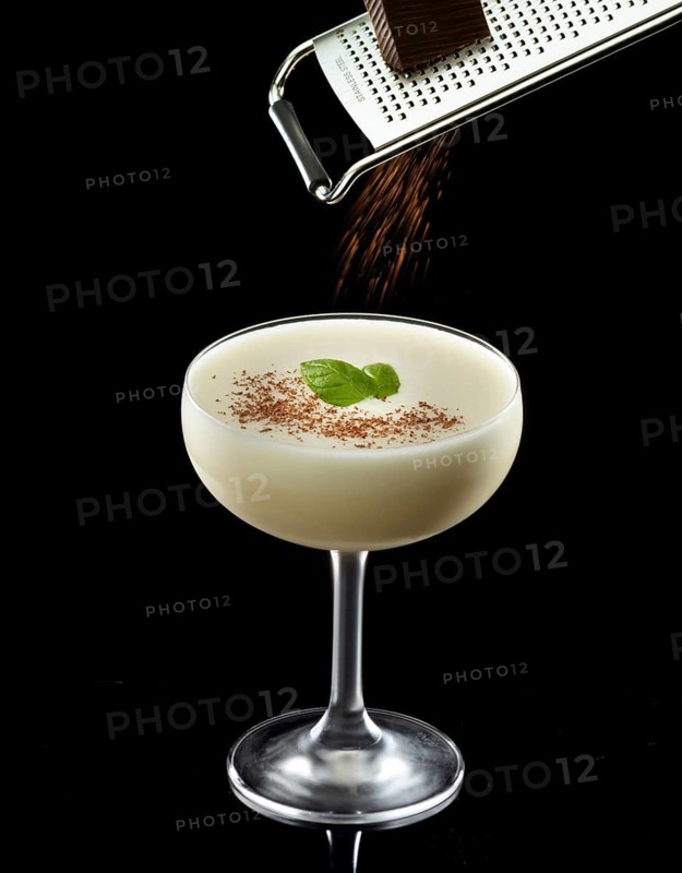 Light cocktail on a black background, grated chocolate and basil leaves as a garnish, studio shot