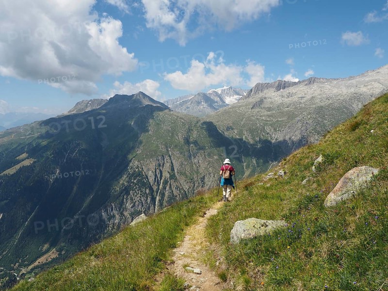Female hiker on a rocky path with wide mountain views and blue sky with clouds, Bellwald, Goms, Canton of Valais, Switzerland