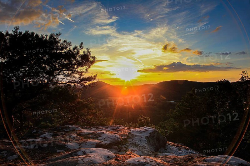 Sunset over wooded hills with clouds in the sky. Rocks in the foreground create a quiet, peaceful atmosphere, Palatinate Forest, sunset, Dahner Felsenland, Palatinate, Germany