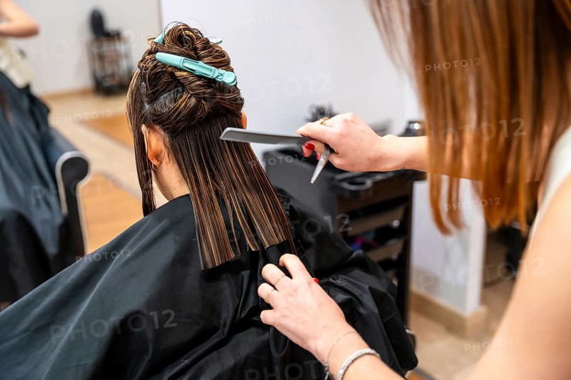 Professional hairdresser trims long wet hair with scissors and comb in a modern salon, close up back view showing skilled hands, care, and a fresh, stylish transformation