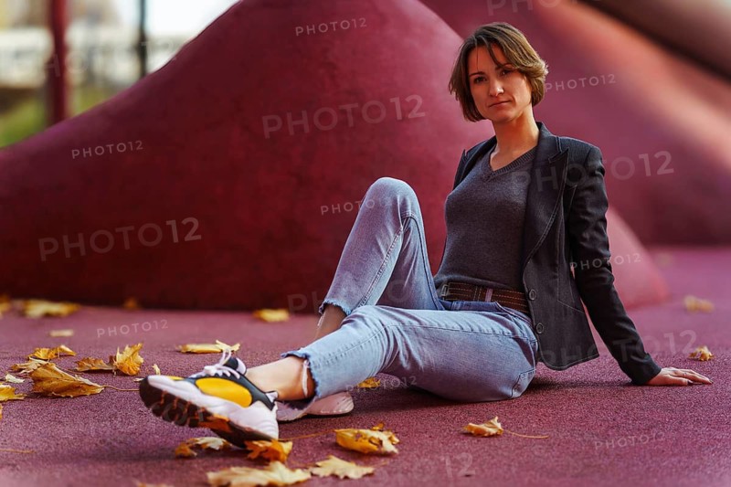 Relaxed young woman sitting among autumn leaves on red background