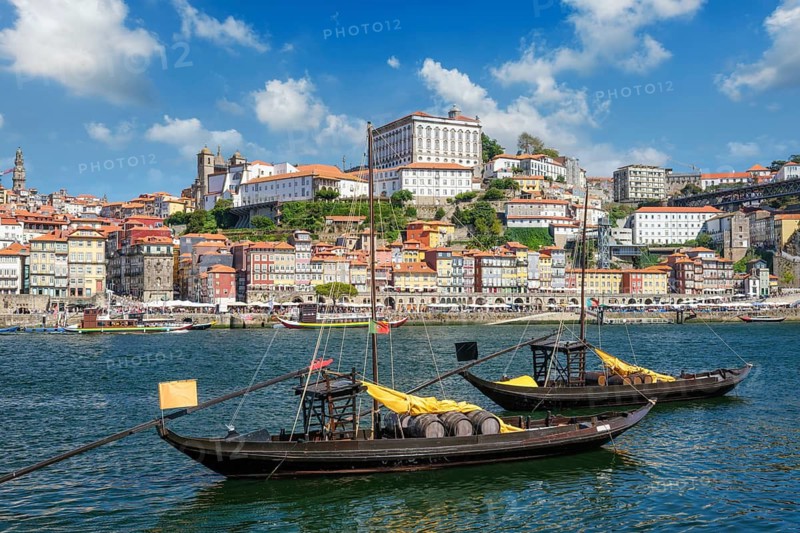 Rabelo boats on Douro River by Porto Ribeira with visible wine company names, barrels and bridge angle near Dom Luis I Bridge
